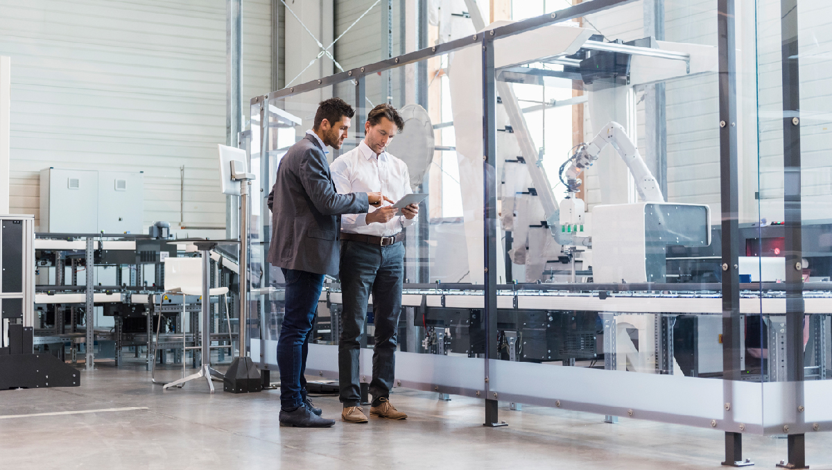 Two businessmen review data on a tablet in a technology factory.