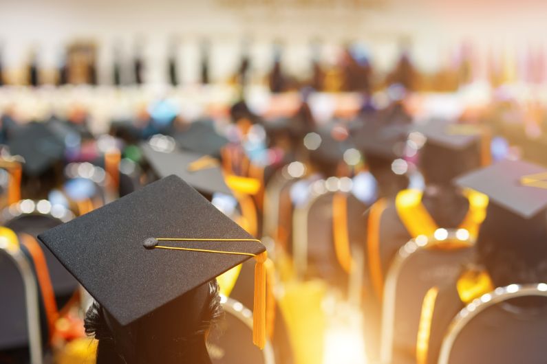 A group of college graduates wearing black caps and gold tassels during an outdoor commencement ceremony.