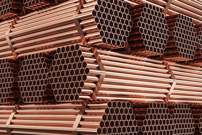 Bundles of long copper pipes secured together and stacked in a large warehouse.