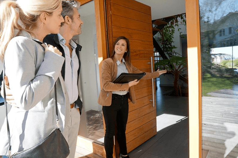 A female realtor smiles and shows the entrance of a new home to potential homebuyers.