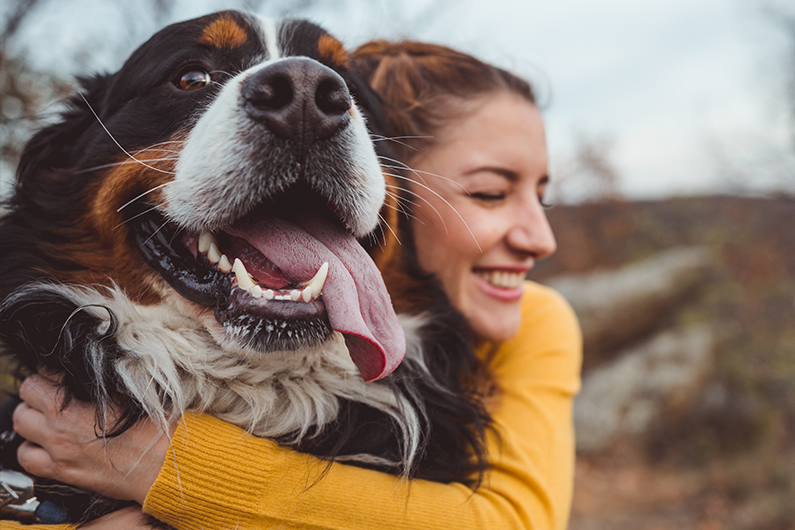 young girl in a yellow shirt hugging her dog at the beach