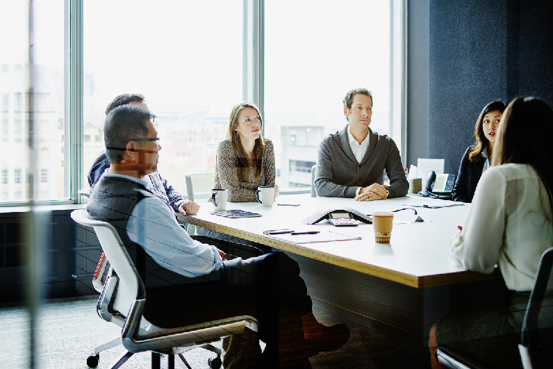 A group of private equity investors sit at a conference table in an office.