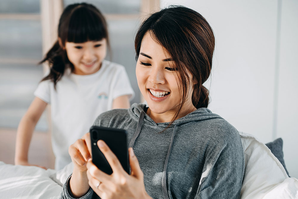 Mother sits with her child and sets up digital wallet apps on her smartphone.